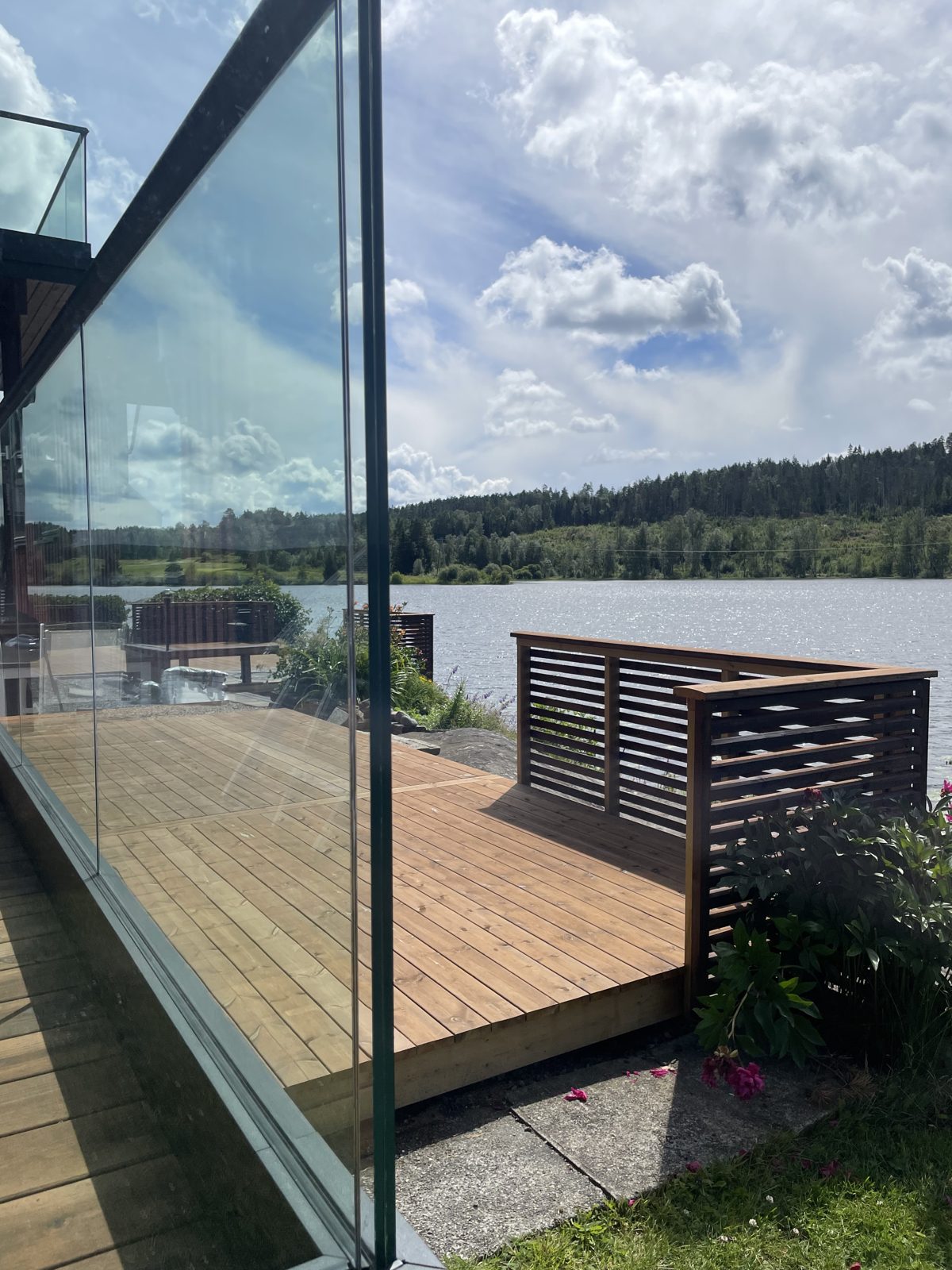 Terrassen ligger tett på vannet, med skjermvegg i spilepanel mot naboside